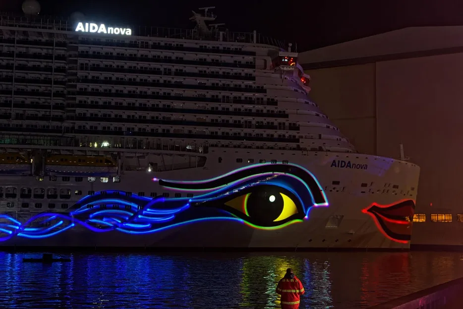 Die AIDAnova bei der Taufnacht in der Meyer Werft: das beleuchtete AIDA-Auge und der Kussmund an der Bordwand spiegeln sich im Hafenbecken