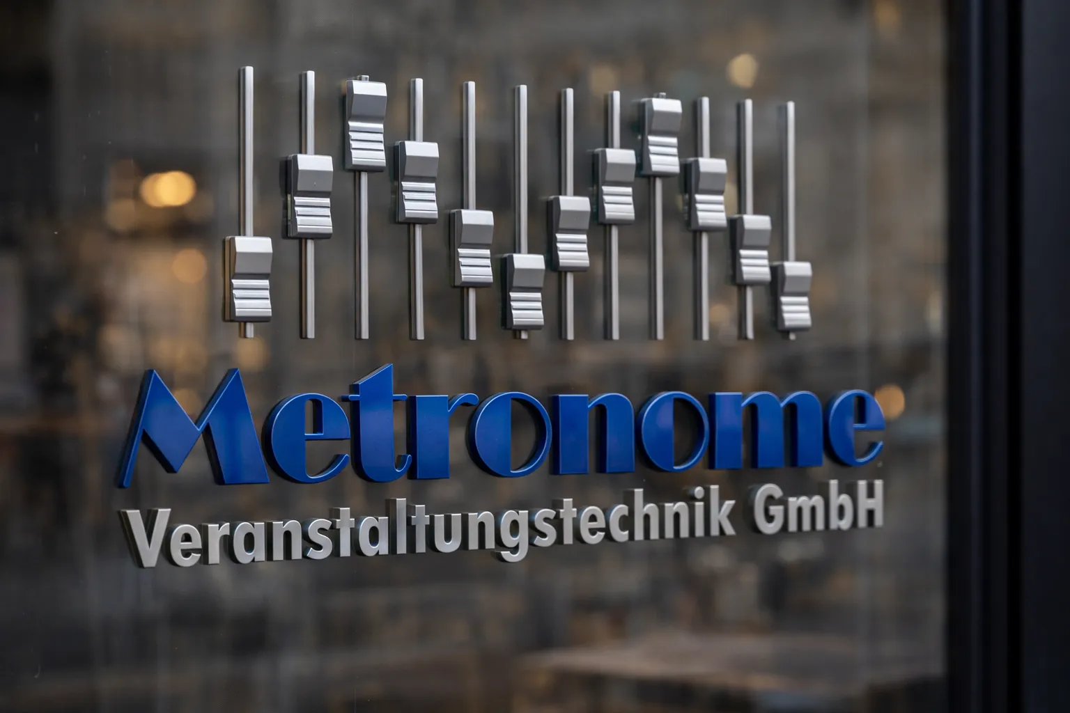 Das Metronome-Logo als 3D-Schriftzug mit Mischpult-Fadern auf einer Glastür