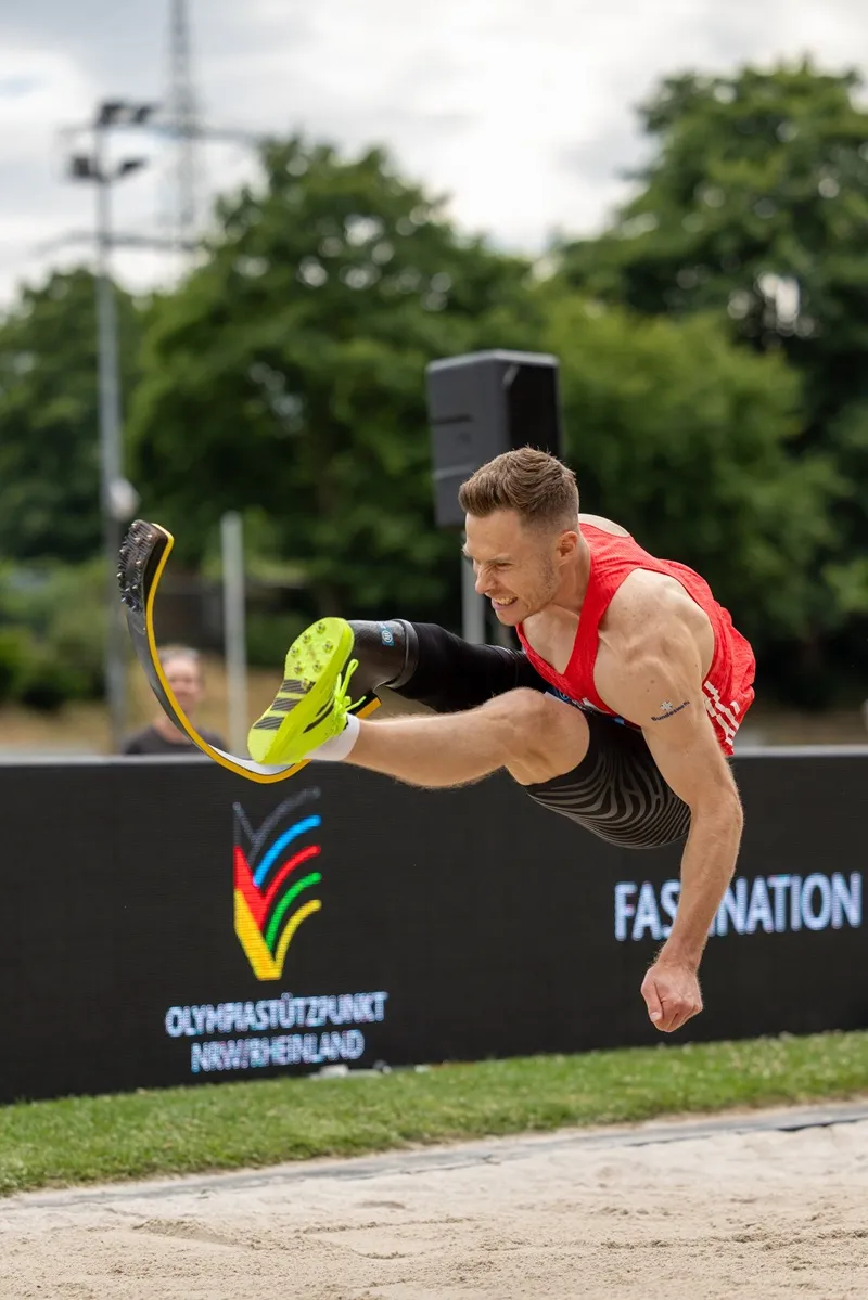 Weitsprung mit Sportprothese, im Hintergrund die Bande des Olympiastützpunkts NRW/Rheinland